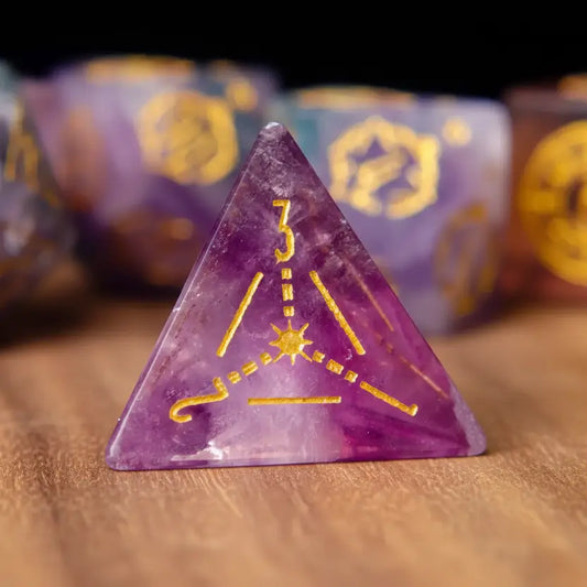 Four-sided D4 gemstone dice in purple fluorite, featuring sharp engraved numerals, highlighted on a walnut wood desk.