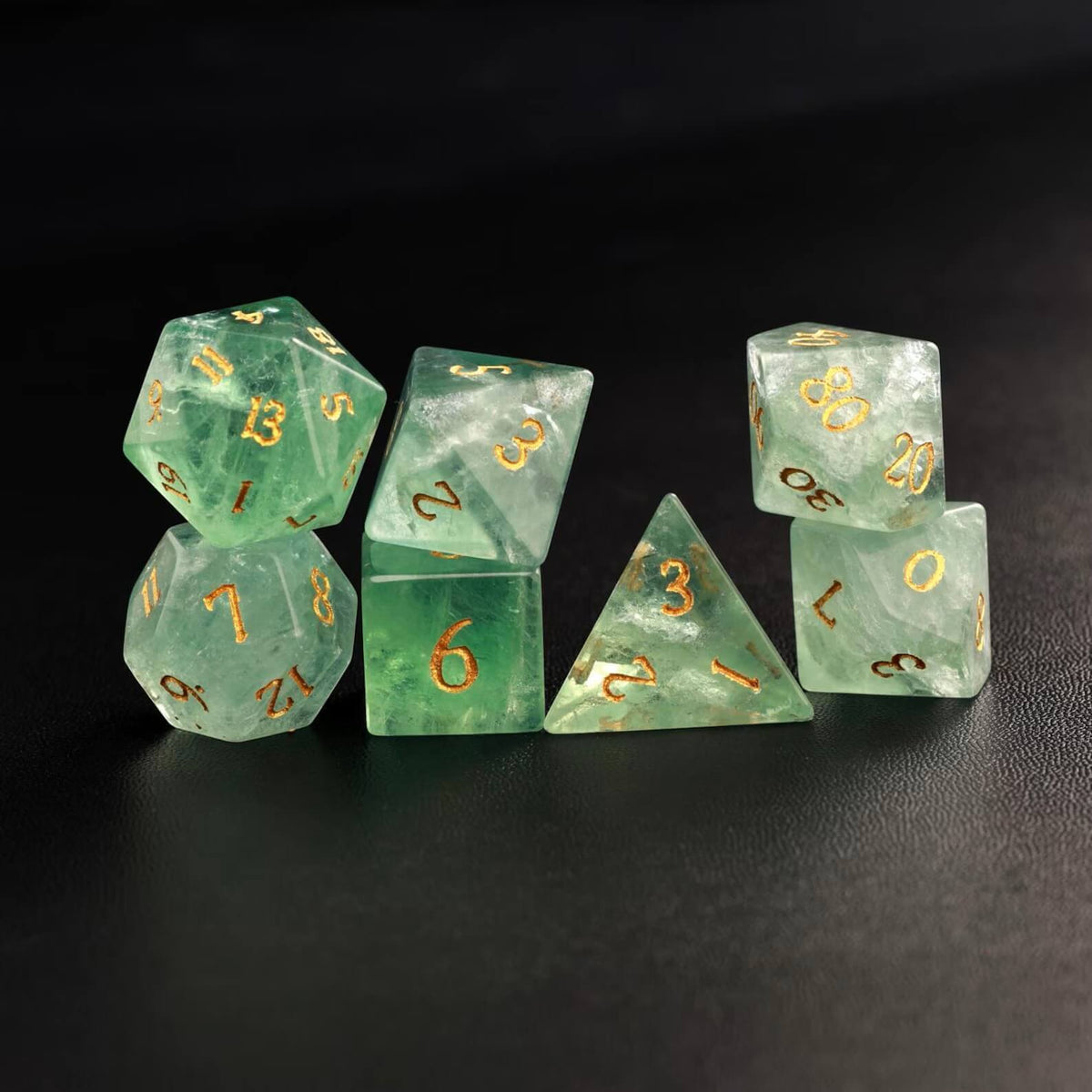 Photo of all 7 polyhedral dice (D4, D6, D8, D10, D%, D12, D20) arranged in a neat line on a dark surface.