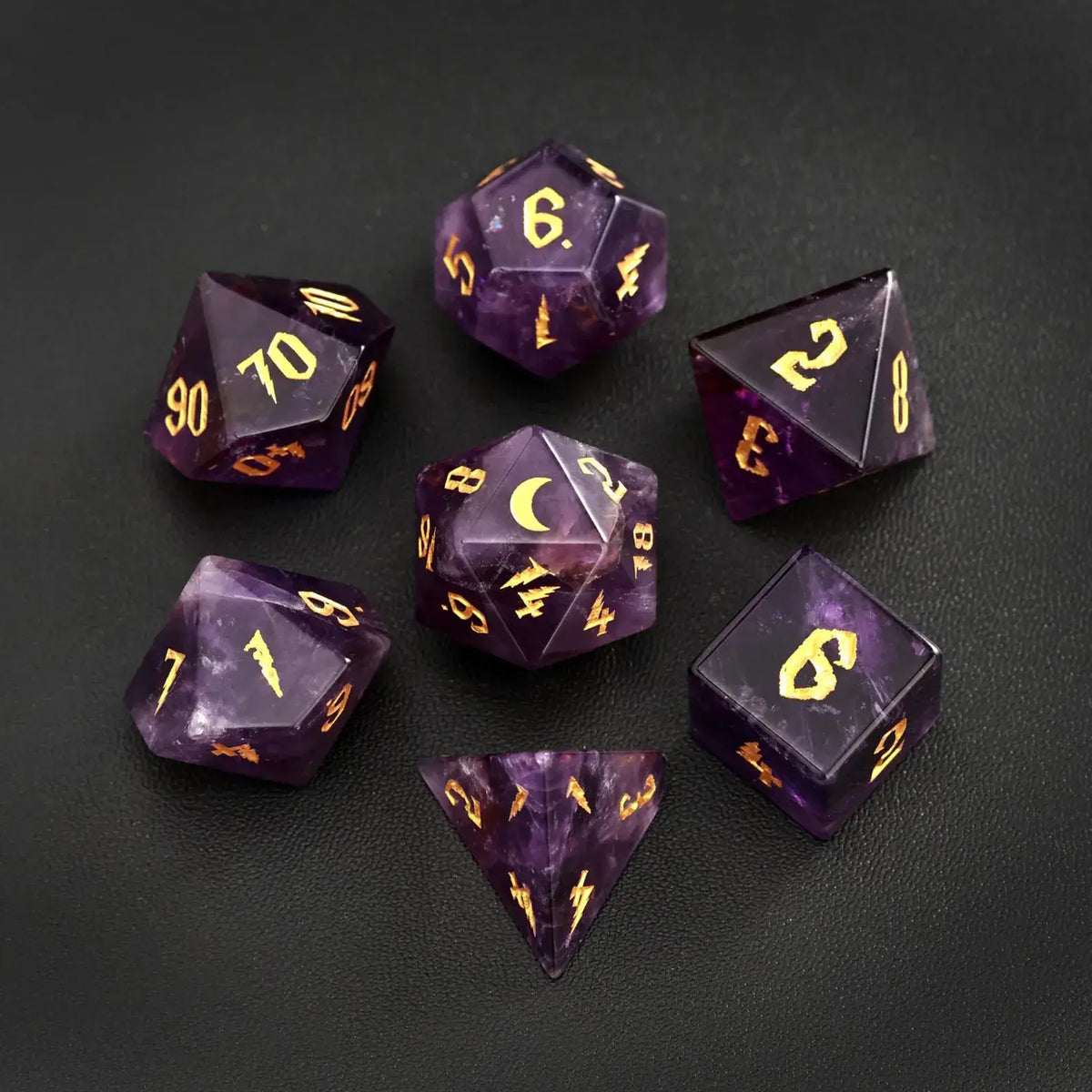 Complete 7-piece set of amethyst gemstone DND dice featuring gold lunar motifs, arranged on a black leather backdrop for a luxury tabletop gaming aesthetic.