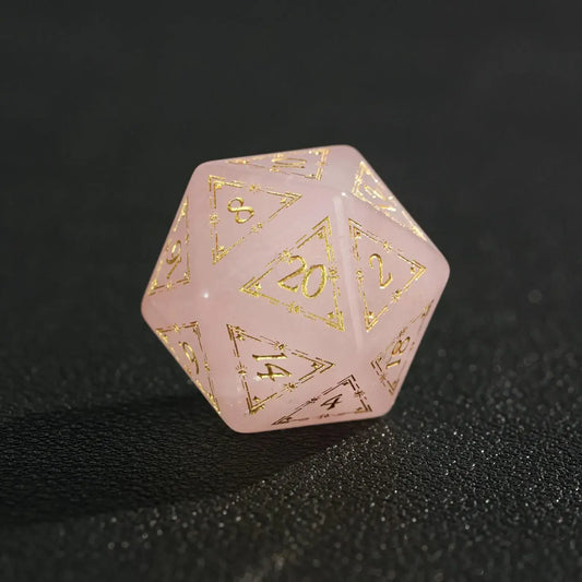 Close-up of engraved pink crystal D20 dice on black, highlighting deep numeric engraving and gem-like clarity