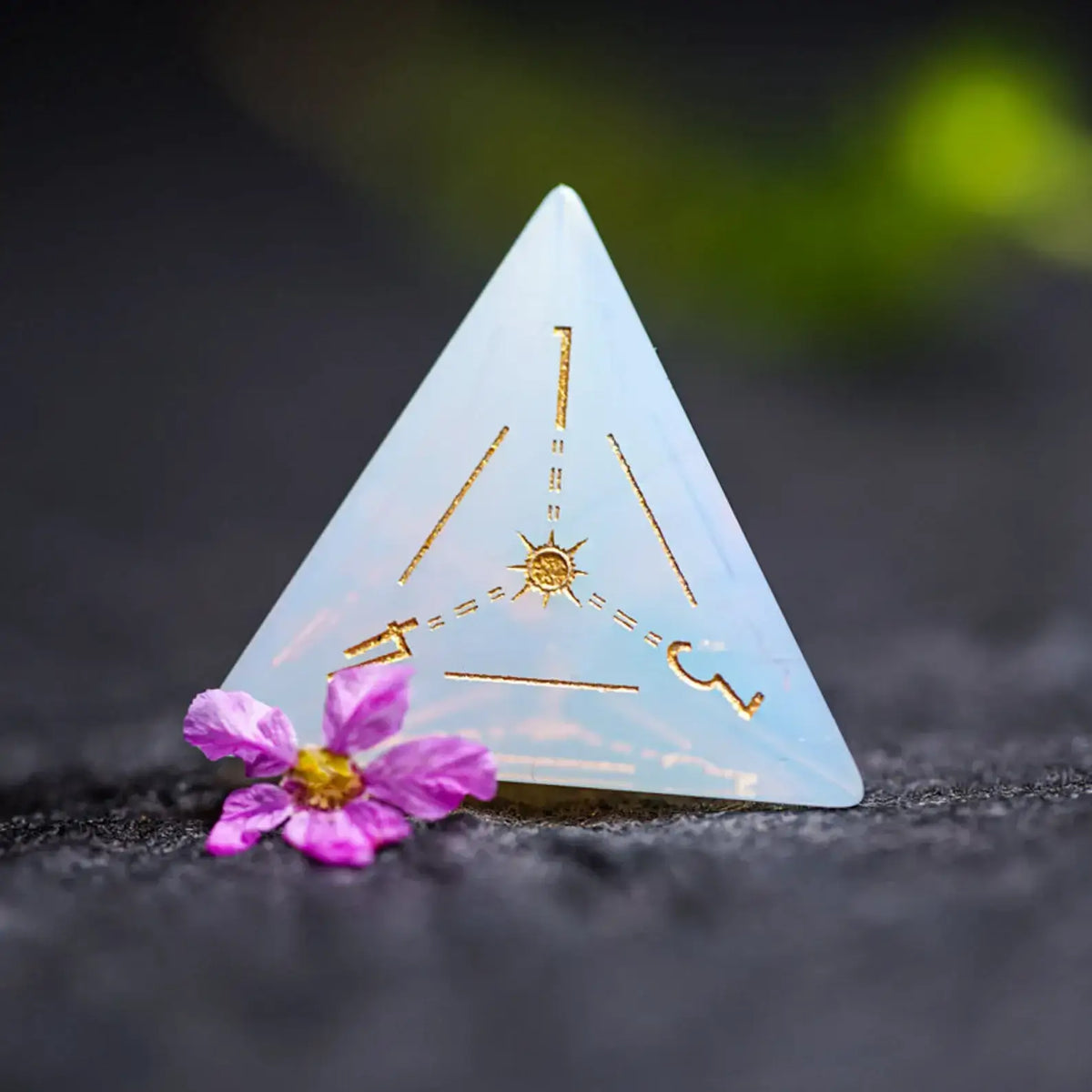 Close-up of an engraved Opalite D4 die with astrology-style geometric patterns.