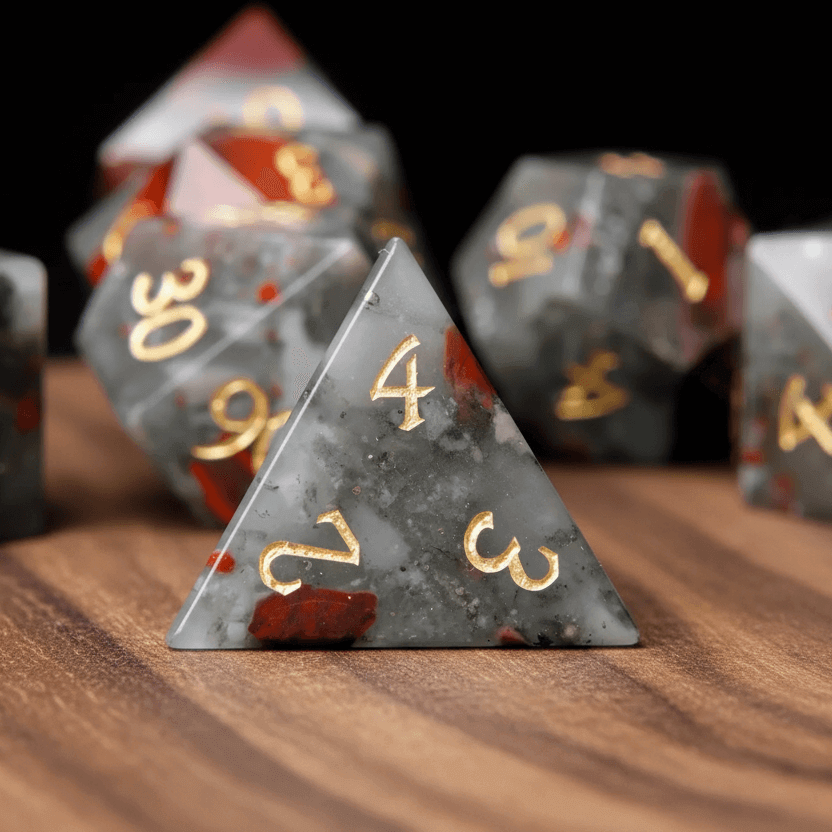 Single pyramid-shaped Grey Bloodstone D4 die standing on a walnut wood table.