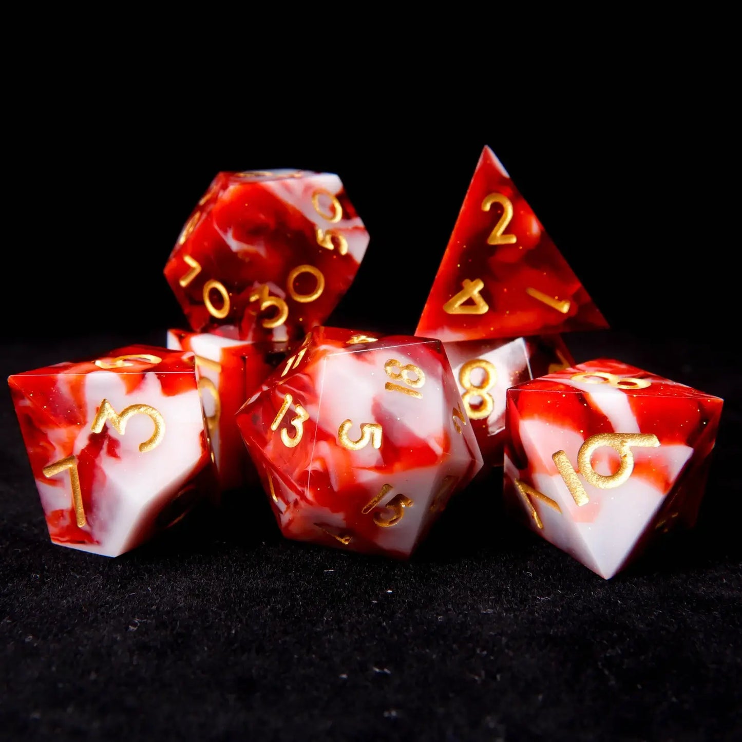 A set of seven red and white resin dice set​ on a black velvet background, adorned with tiny white glitters like snowflakes.