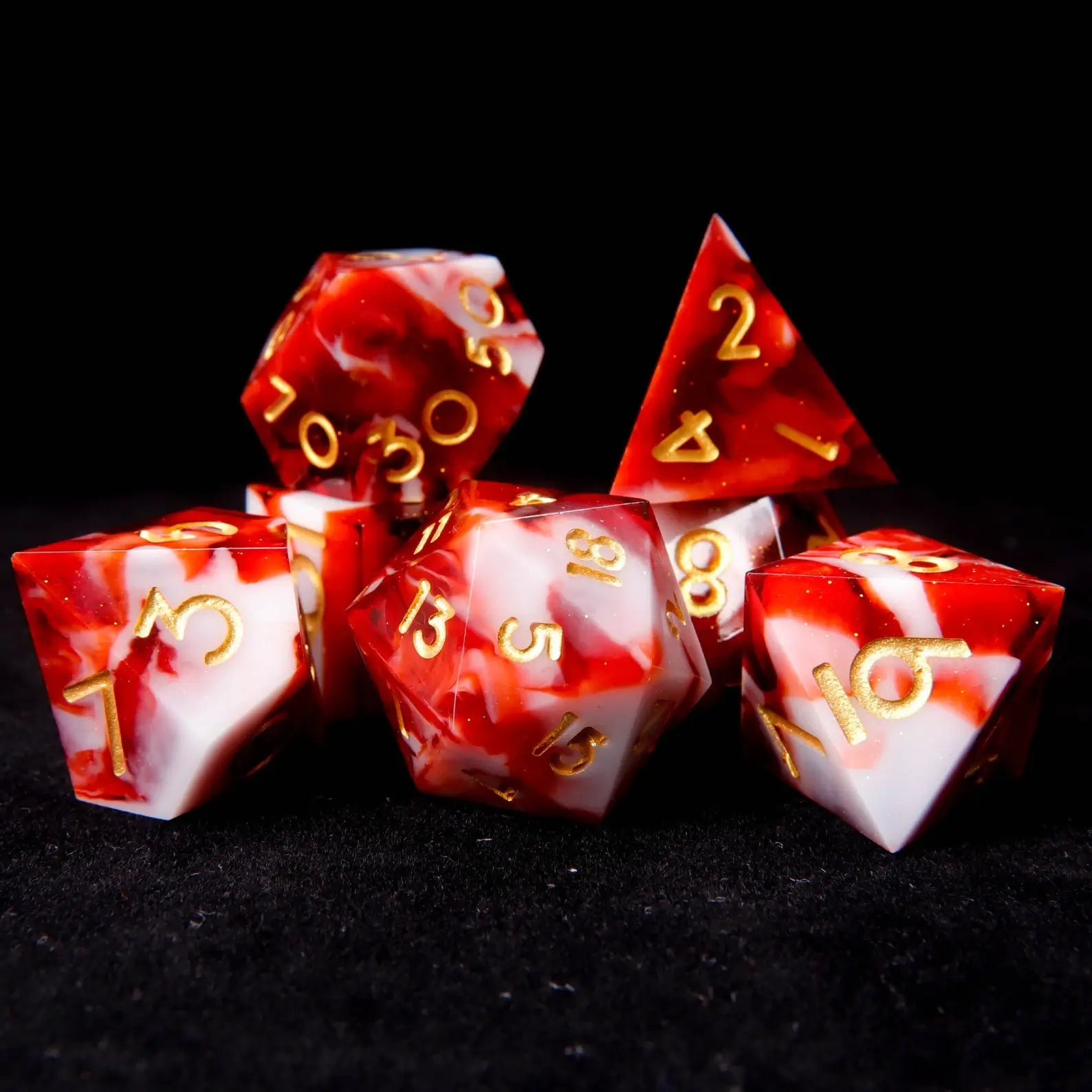 A set of seven red and white resin dice set​ on a black velvet background, adorned with tiny white glitters like snowflakes.