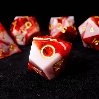 A red and white resin D10 stands on a black velvet background, adorned with tiny white sequins like snowflakes. Next to it is a stand-up, customizable laser-engraved personalized DND tin box.