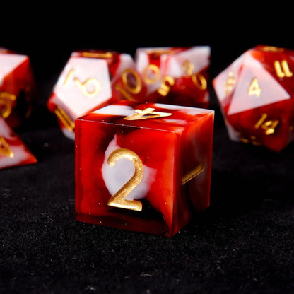 A red and white resin D6 is placed on a black velvet background, adorned with small white sequins like snowflakes.