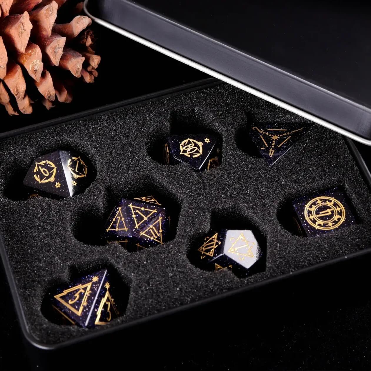 A set of seven blue sandstone gemstone-carved dice on a black background is housed in an iron box lined with black sponge.