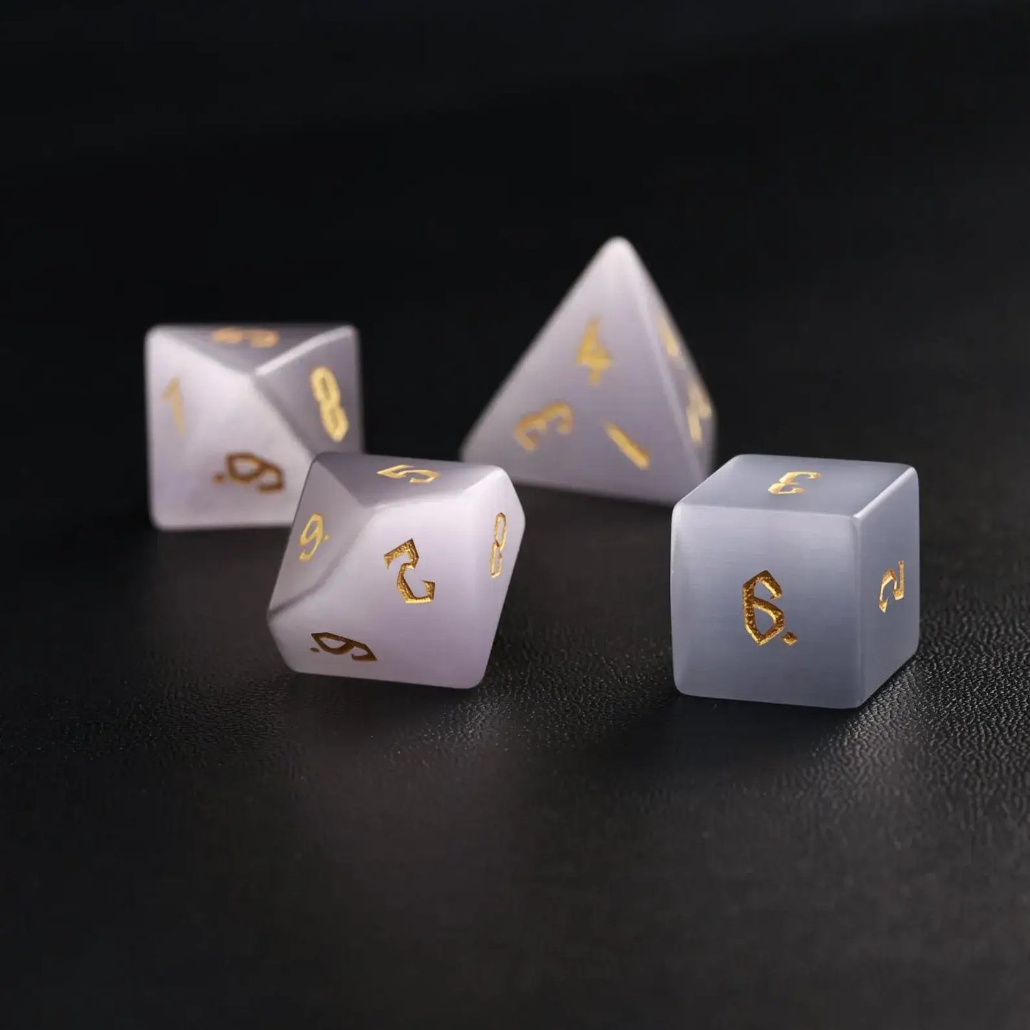 Elegant arrangement of four Grey Cat's Eye Dice (D4, D6, D8, D12) on a solid black background, showcasing the understated grey color and luminous shine.