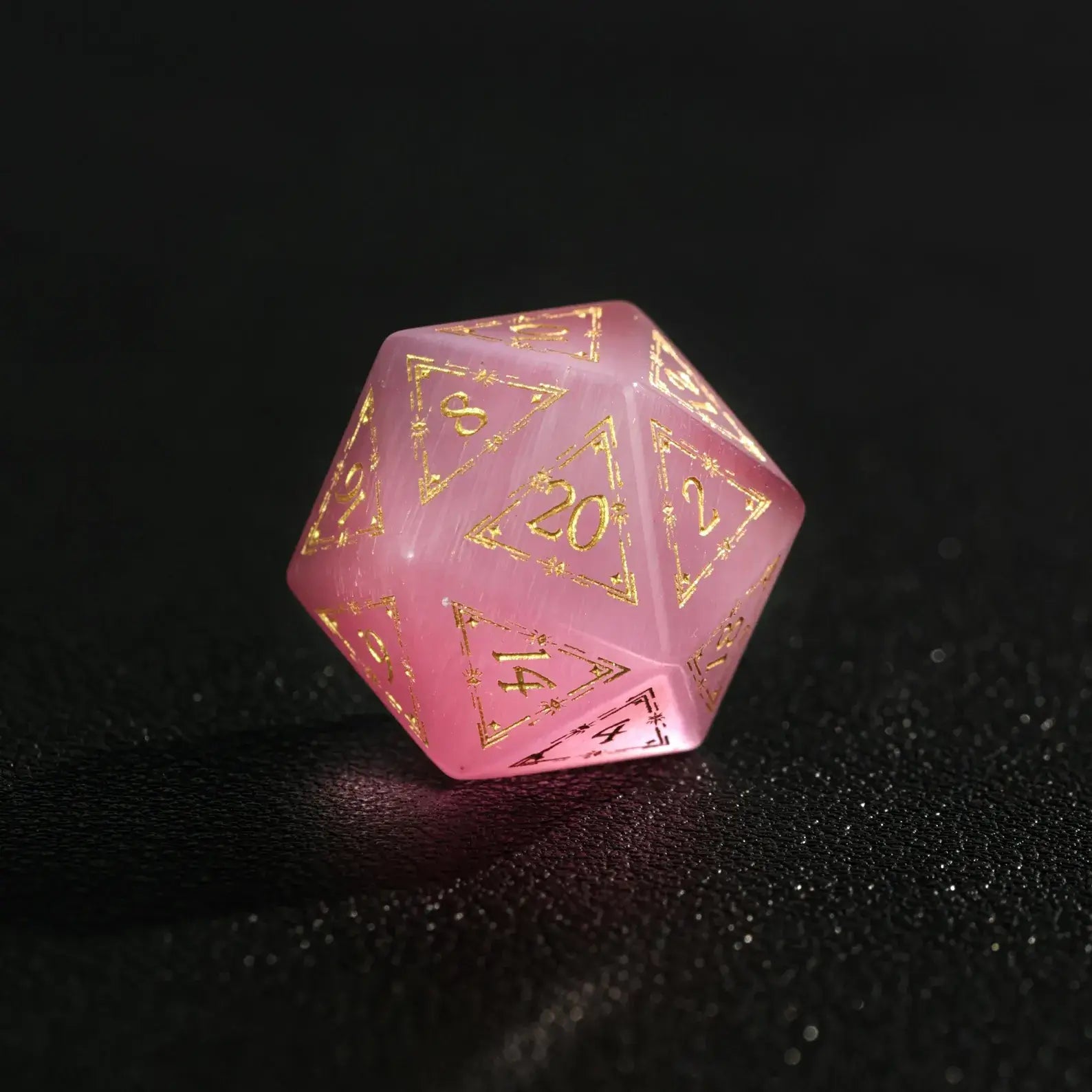 Close-up of a single Pink Cat's Eye Gemstone Dice D20, a handcrafted DND polyhedral die on a dark black background, highlighting the distinct cat's eye light effect.