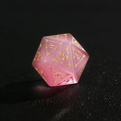 Close-up of a single Pink Cat's Eye Gemstone Dice D20, a handcrafted DND polyhedral die on a dark black background, highlighting the distinct cat's eye light effect.