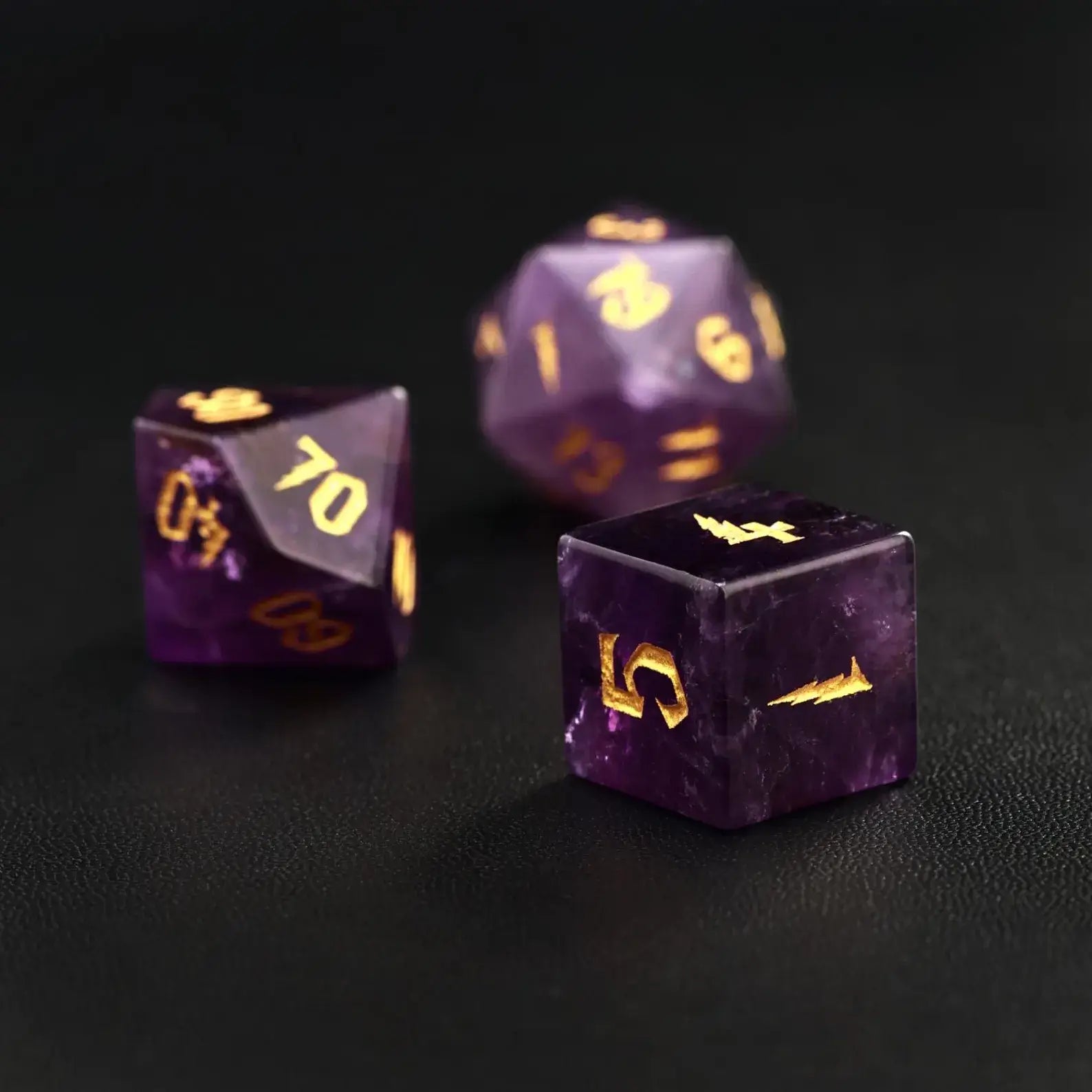 Three hand-carved amethyst crystal dice for RPG gaming, featuring intricate gold celestial engravings and natural stone texture.