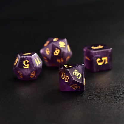 Four semi-precious amethyst gemstone dice on black leather, showcasing the natural violet hues and premium gold engraving.