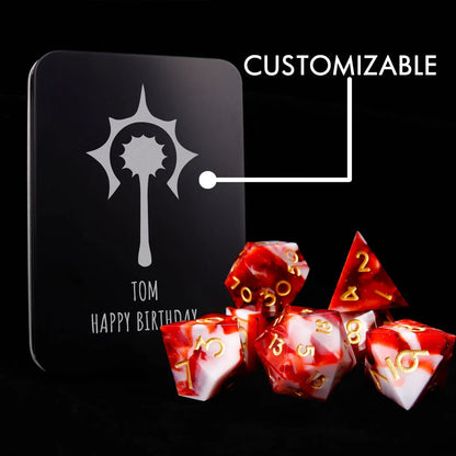 A set of seven red and white resin dice sits on a black velvet background, adorned with tiny white sequins resembling snowflakes. Next to it stands a personalized DND tin box that can be custom-laser-engraved.