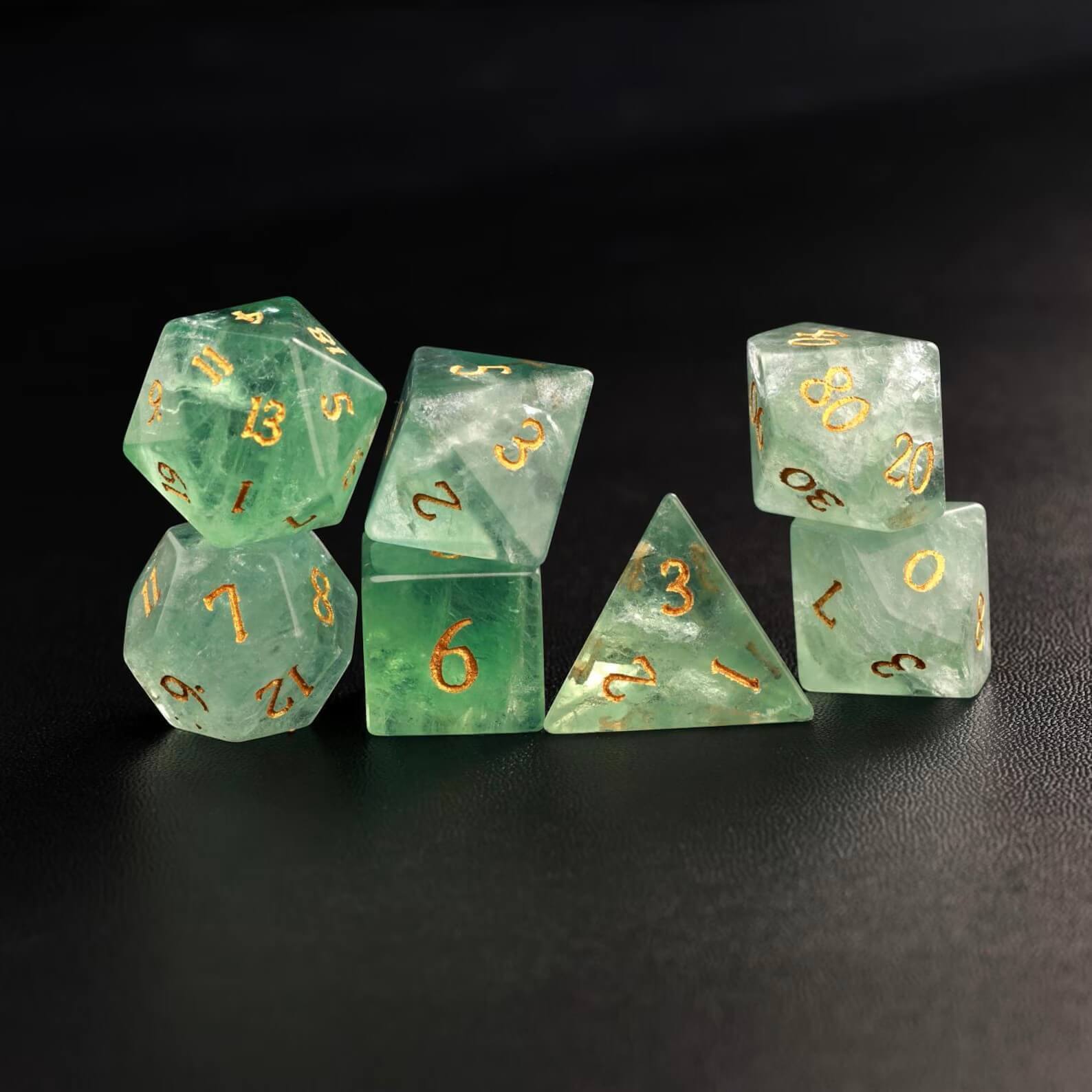 Photo of all 7 polyhedral dice (D4, D6, D8, D10, D%, D12, D20) arranged in a neat line on a dark surface.
