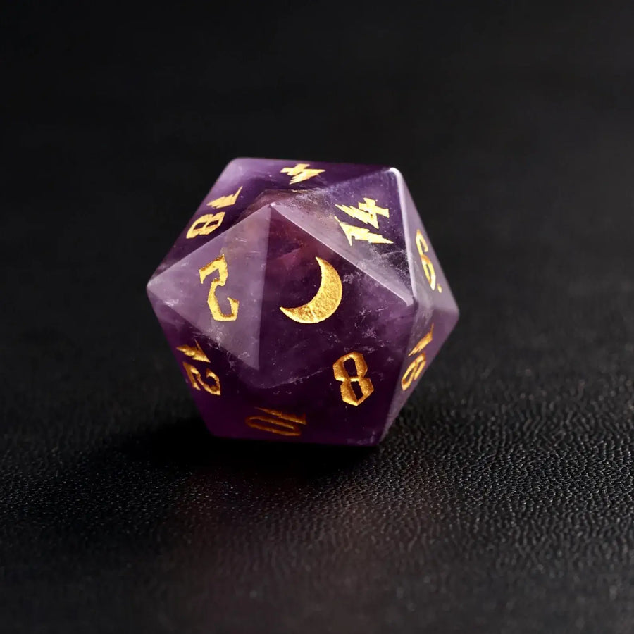 Close-up of a single natural amethyst D20 die with gold moon engravings and numbers on a premium black leather surface.