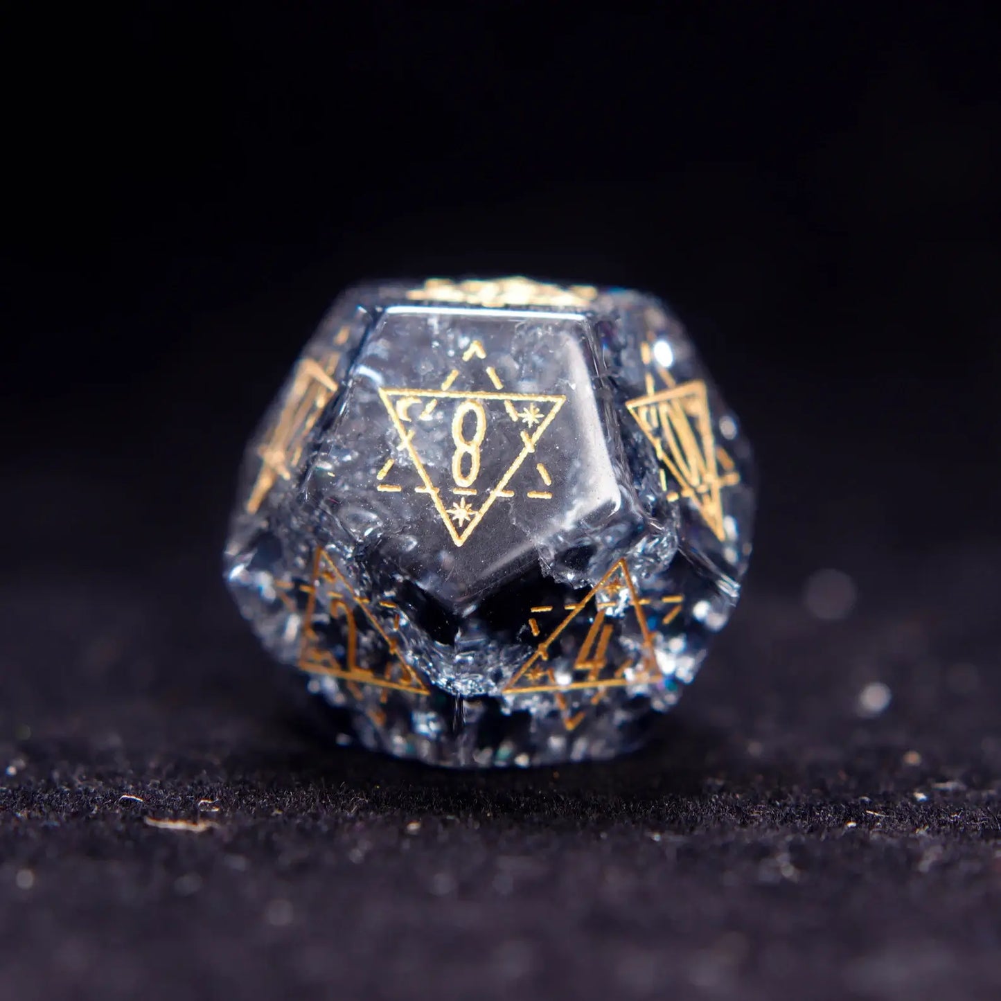 Single Black Crystal D12 dice with sharp edges and gold numbers, isolated on dark background