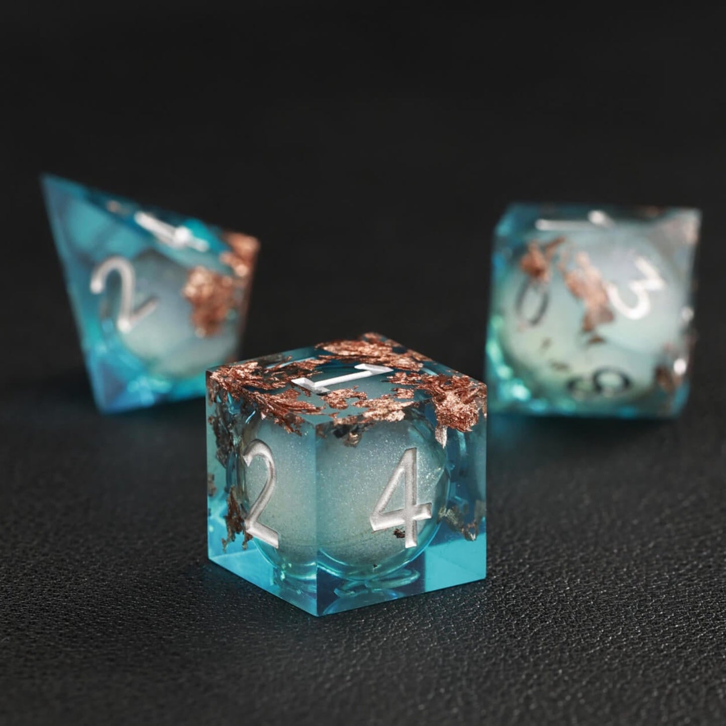 Close-up of Blue Copper Foil Liquid Core D4 resin dice with shimmering core and sharp edges