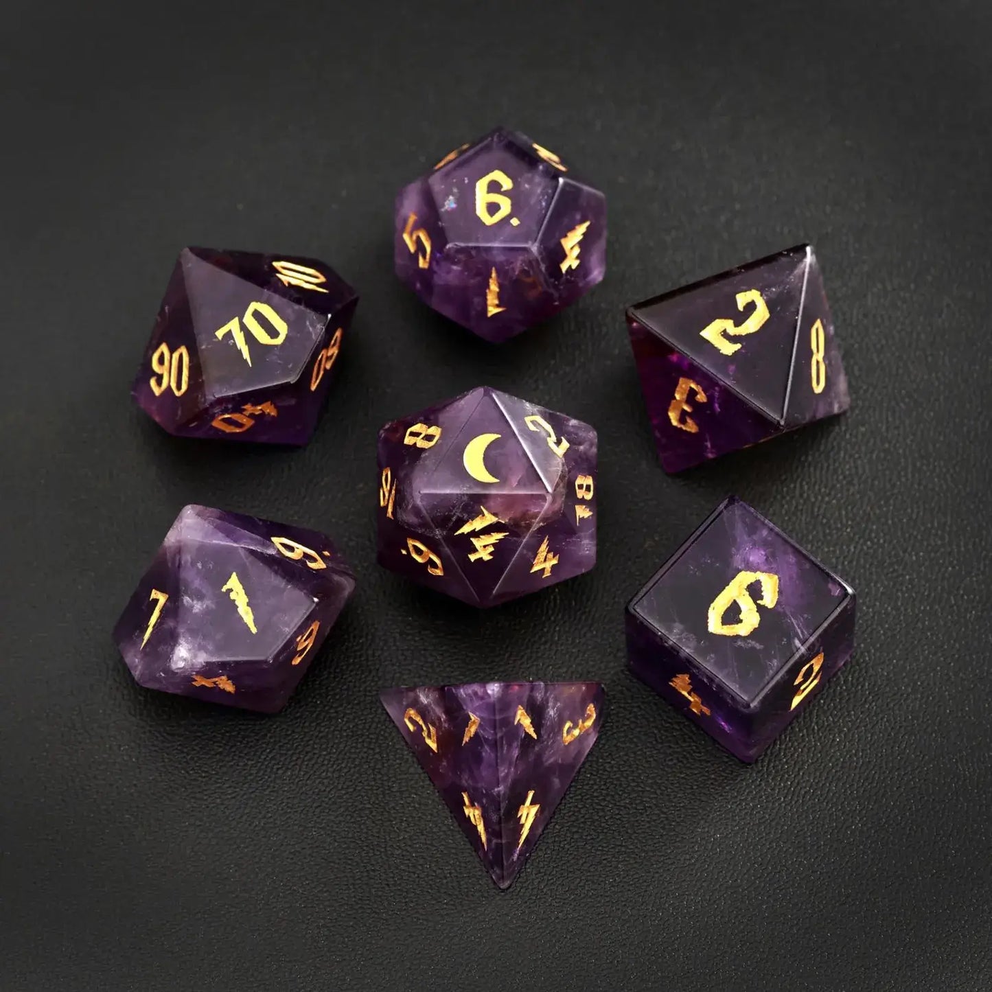Complete 7-piece set of amethyst gemstone DND dice featuring gold lunar motifs, arranged on a black leather backdrop for a luxury tabletop gaming aesthetic.