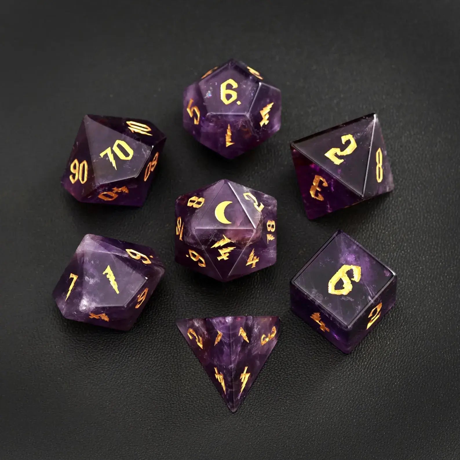 Complete 7-piece set of amethyst gemstone DND dice featuring gold lunar motifs, arranged on a black leather backdrop for a luxury tabletop gaming aesthetic.