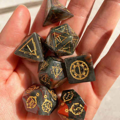 A carefully held Bloodstone Gemstone Engraved Dice Set in natural daylight, highlighting the stone's deep green hues and sharp edges against skin tones