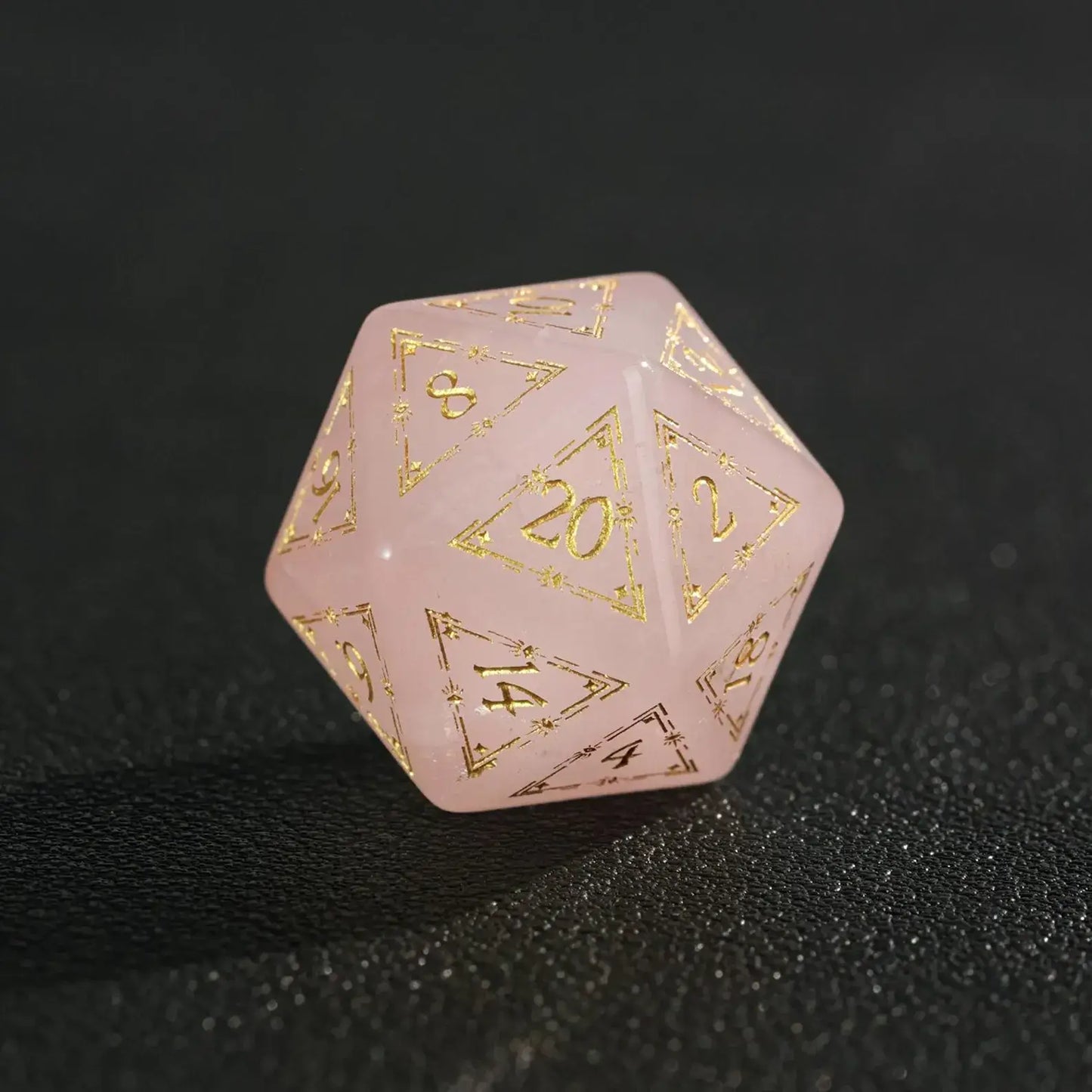 Close-up of engraved pink crystal D20 dice on black, highlighting deep numeric engraving and gem-like clarity