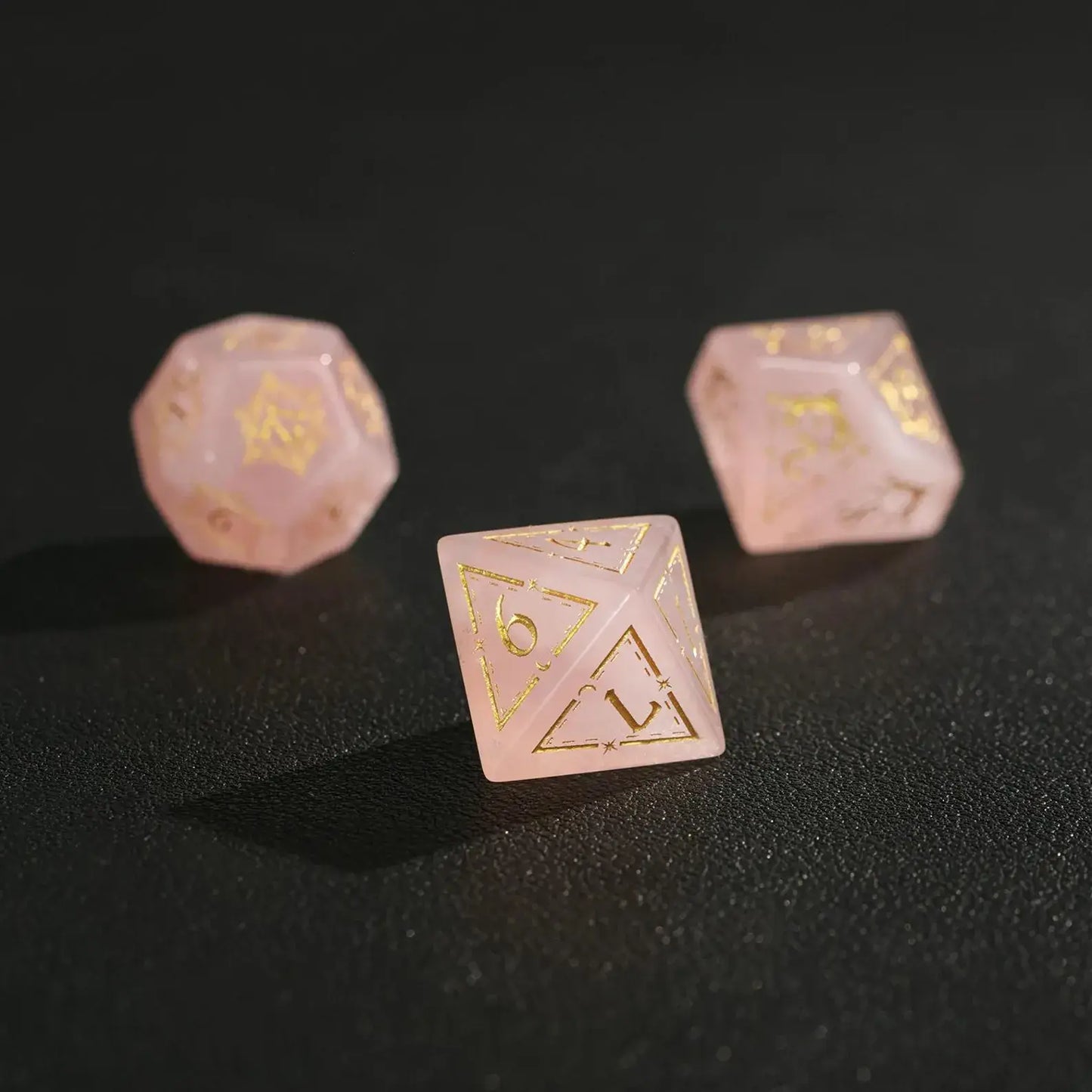Artistic arrangement of three Pink Crystal dice (D4, D10, D12) on a dark background, forming a simple still life.