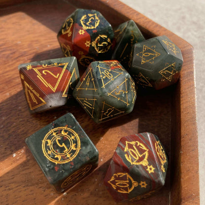 Full set of engraved Bloodstone dice presented on a rustic walnut wood tray in soft natural light, emphasizing organic texture and premium feel

